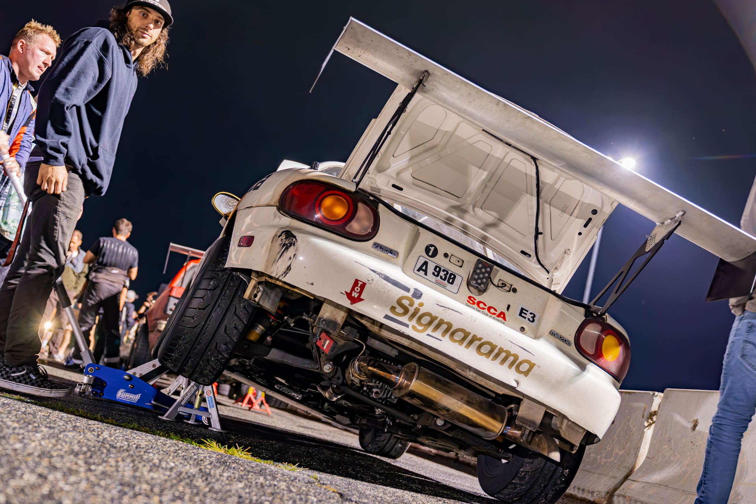 The car up on jacks in the paddock after dark, crew working under floodlight.