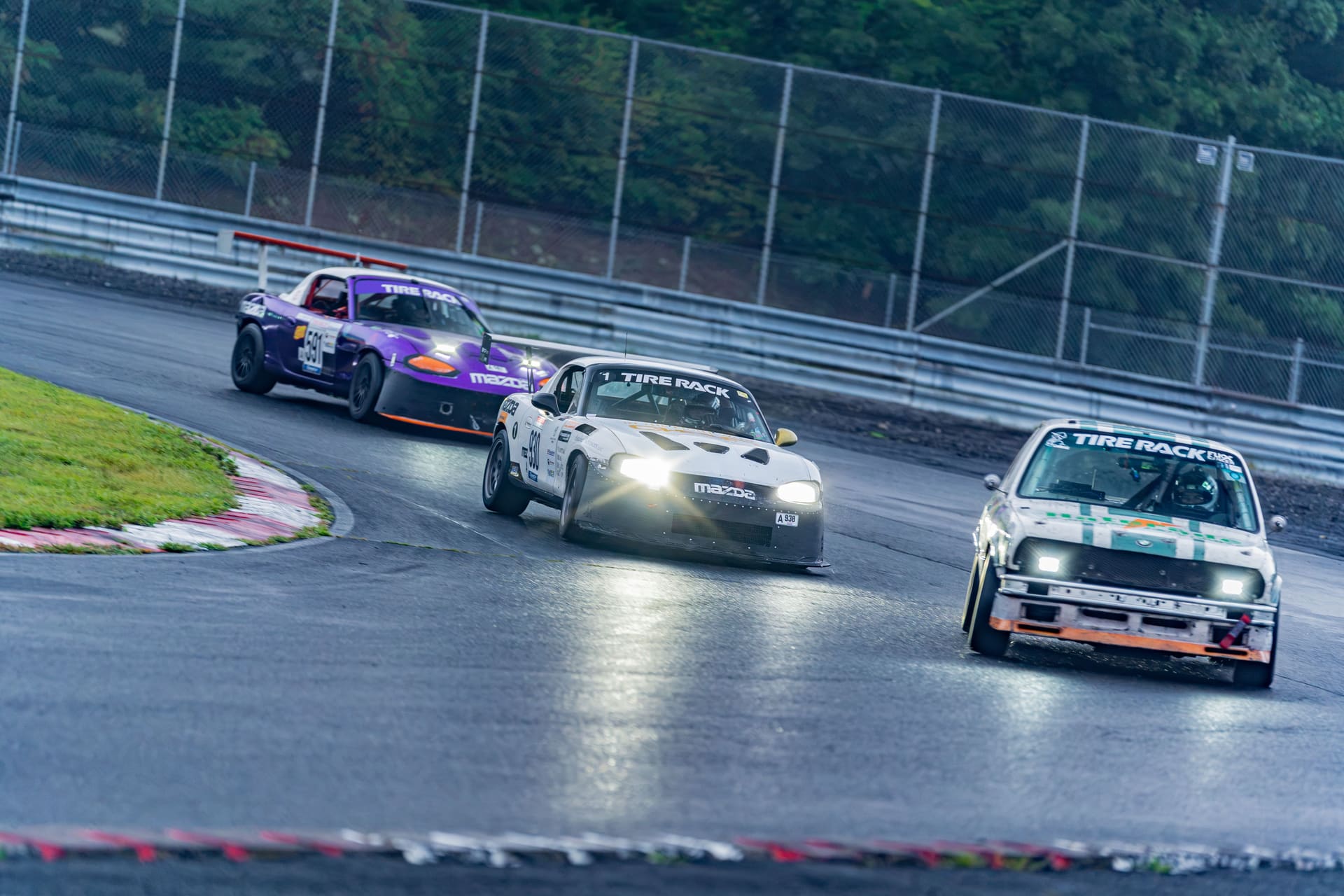 Three cars nose to tail under lights in the wet.